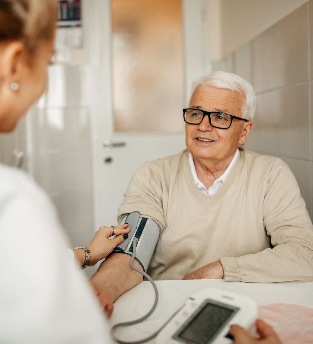 Pflegekraft misst bei einem Senior zu Hause den Blutdruck