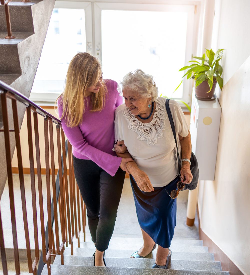 Pflegekraft begleitet eine Seniorin im Treppenhaus